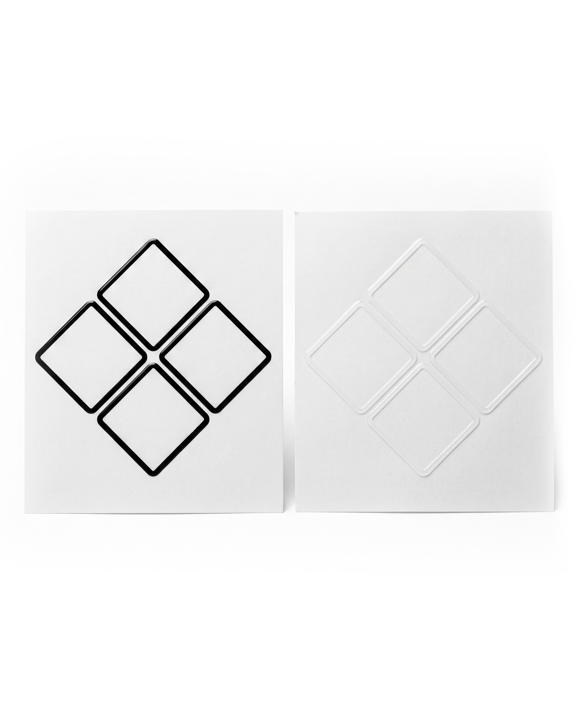 A pair of square white decals or stickers shown side by side on a white background. The left sticker features a black outline of four connected diamond shapes, while the right sticker shows the corresponding white recessed or embossed diamond pattern.