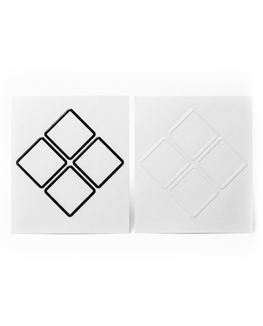A pair of square white decals or stickers shown side by side on a white background. The left sticker features a black outline of four connected diamond shapes, while the right sticker shows the corresponding white recessed or embossed diamond pattern.