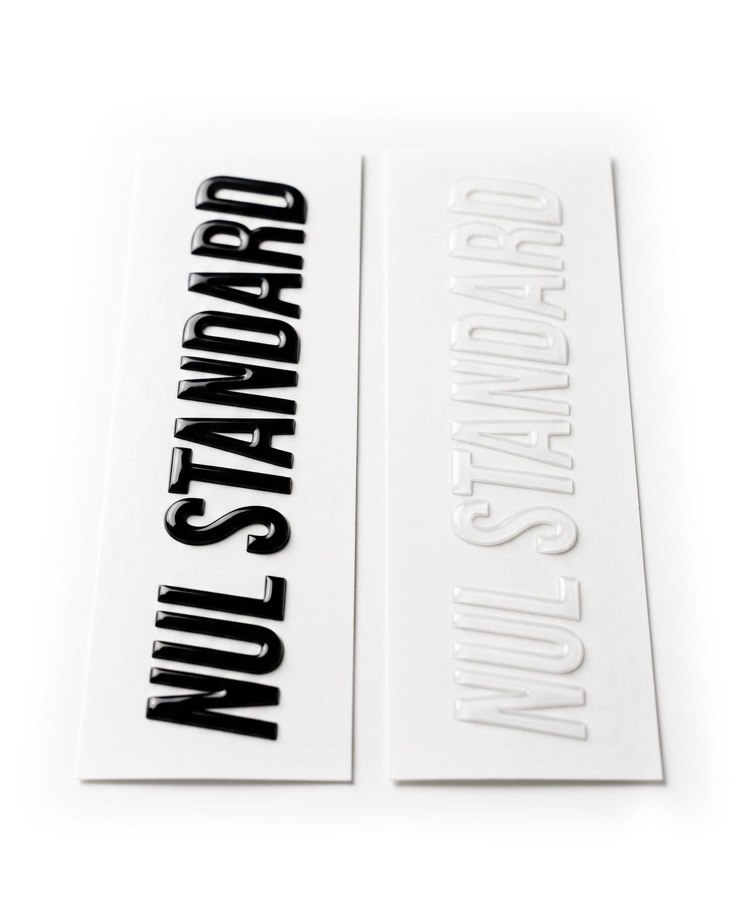 Two rectangular decals or stickers on a white background, one printed with the words 'NUL STANDARD' in bold black and the other in raised white.