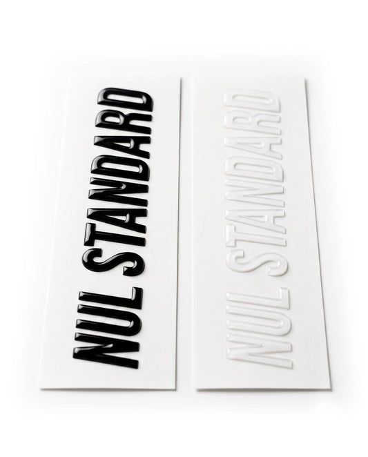 Two rectangular decals or stickers on a white background, one printed with the words 'NUL STANDARD' in bold black and the other in raised white.