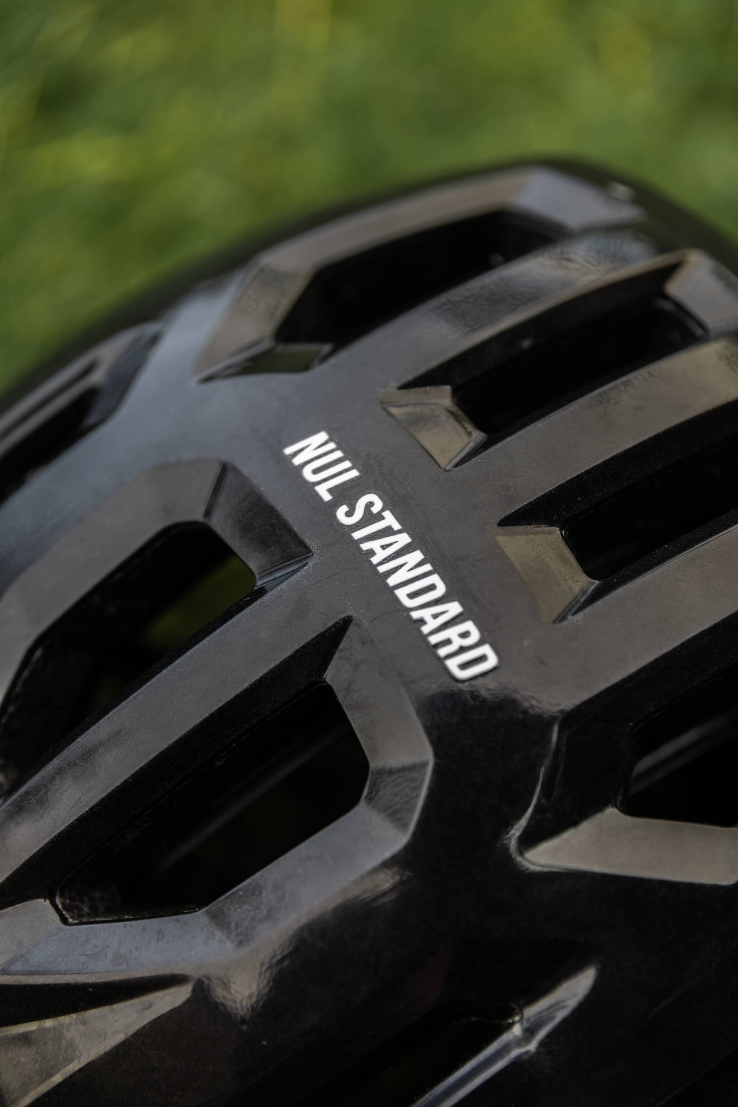 Close-up of a black bicycle helmet with the brand name 'NUL STANDARD' printed in white on the side, set against a blurred green outdoor background.